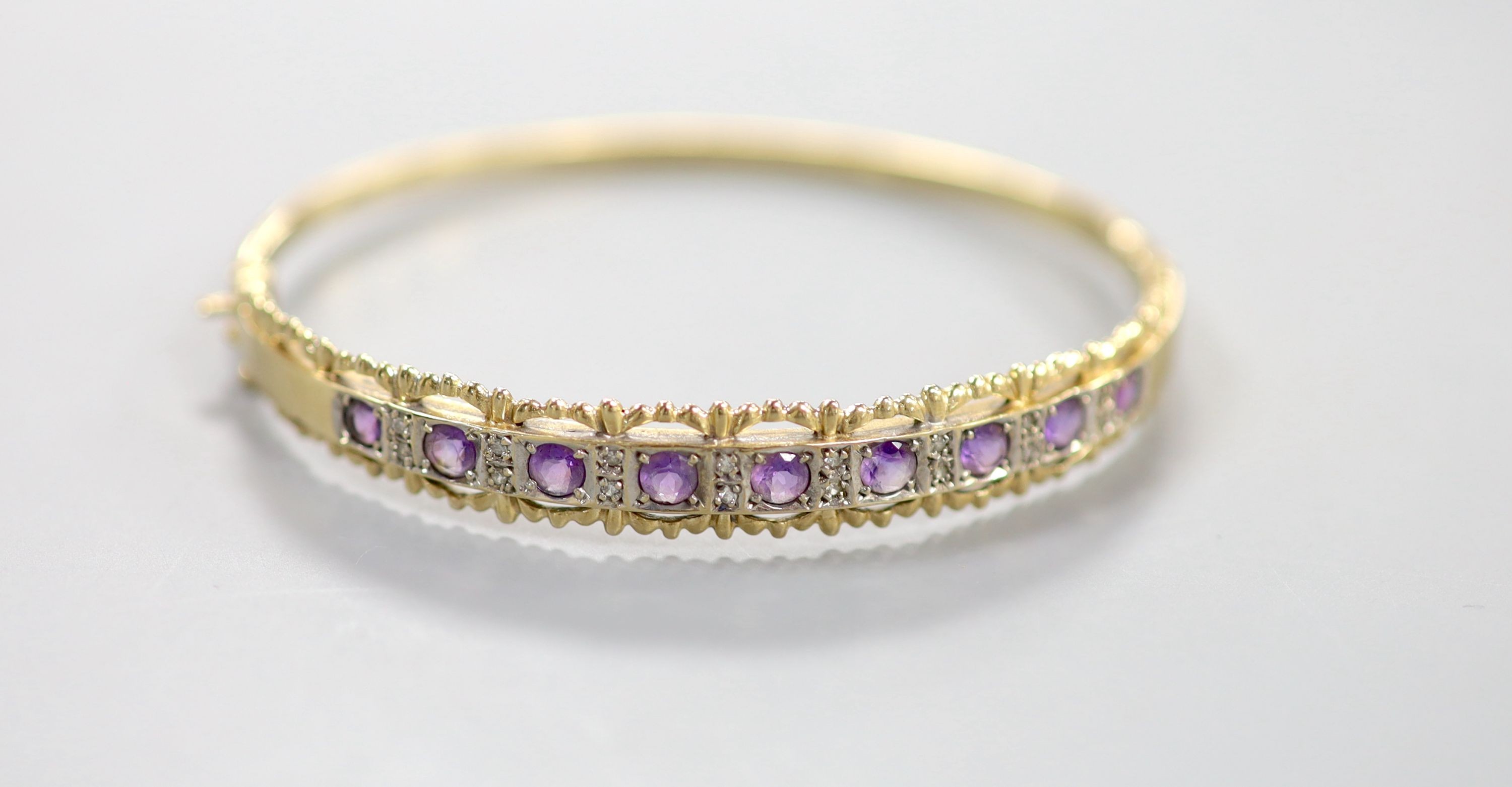 A modern 9ct gold and graduated nine stone amethyst set bracelet, with diamond chip set spacers, interior diameter approx. 56mm, gross 11.3 grams.